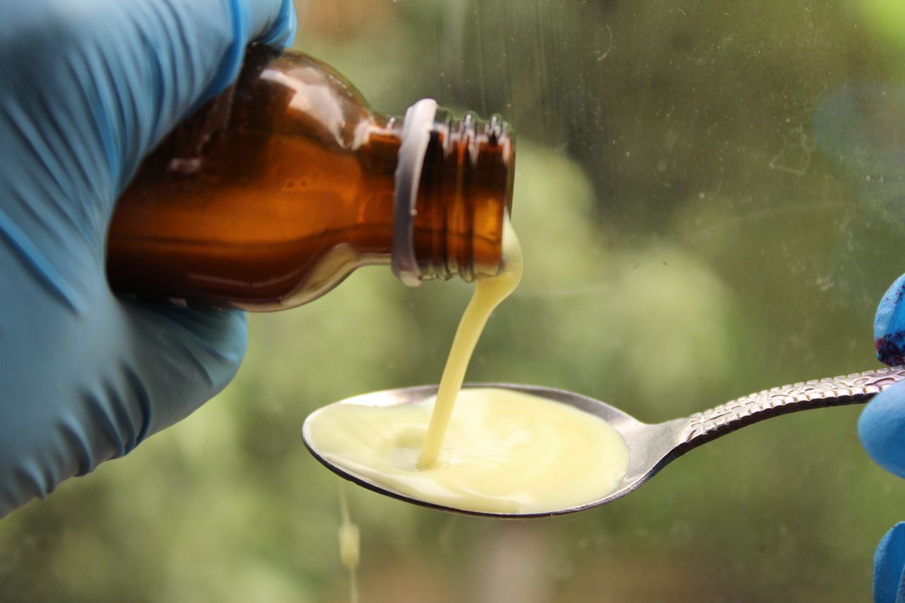 Menu A gloved hand pours liquid medication from a brown bottle into a spoon.